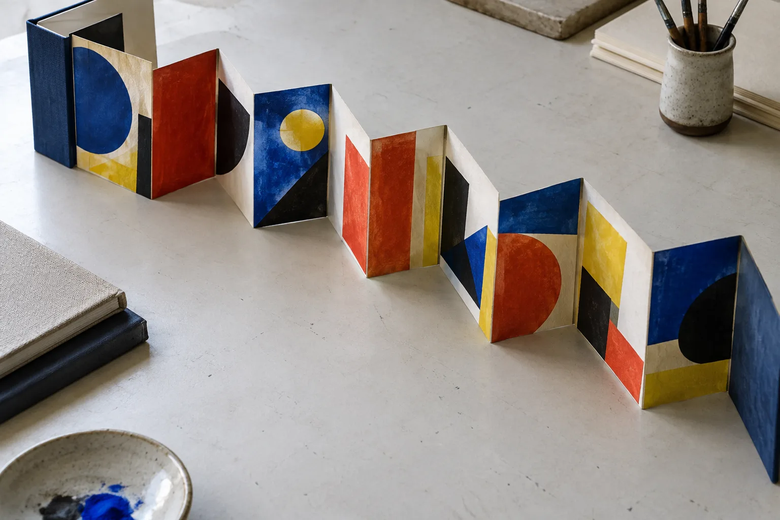 Livre accordéon ouvert sur une table, composé de plis successifs et de formes géométriques colorées.